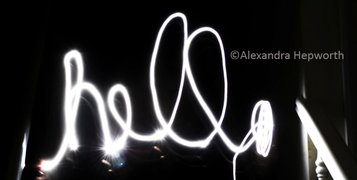 Lightpainting photo by Alexandra Hepworth writing the word 'hello' in black background by some stairs.