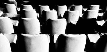 Black and white  photo of white chairs in repetition in an outside amphitheatre. Photo by Eva Kalpadaki.