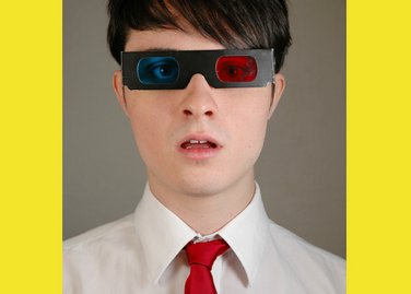 Portrait photo of a young man from shoulders and above, with red tie and 3D blue and red glasses with a yellow border. Photo by Eva Kalpadaki.
