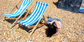 Female student taking photos of the white and blue stripey deck chairs on the Brighton seafront while lying down on the pebbles. Photo by Eva Kalpadaki.