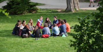 A circle of people sitting on the grass in a park and discussing.